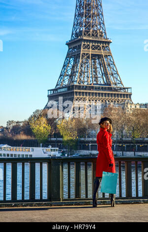 Hell in Paris. In voller Länge Portrait von glücklich trendige Frau im roten Mantel stehen am Ufer in Paris, Frankreich Stockfoto