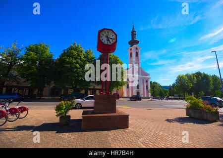 Otocac Town Clock auf dem Stadtplatz (Trg) mit Holy Trinity Church im Hintergrund auf einem sonnigen Nachmittag/Abend Stockfoto