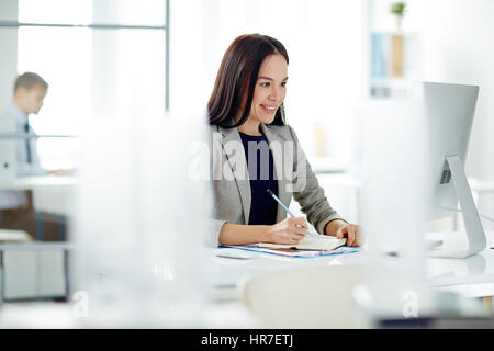 Porträt des erfolgreichen asiatischen Geschäftsfrau beschäftigt, arbeiten am Schreibtisch im modernen Büro, Notizen im Planer und Computer-Bildschirm betrachten Stockfoto