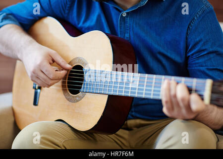 Nahaufnahme der Mann sitzt auf bequemen Sessel und üben in spielt akustische Gitarre Stockfoto