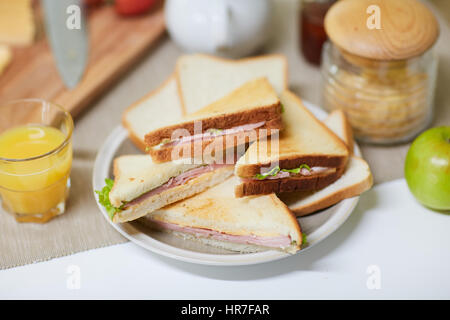 Nahaufnahme der appetitlichen Frühstück vorbereitet für Familie: Sandwiches mit Schinken und Salat, Apfel, Glas Orangensaft, Glas mit Getreide und schneiden Stockfoto