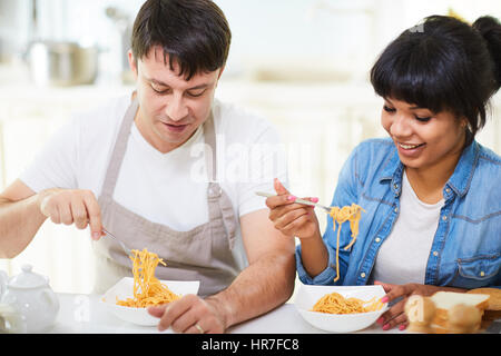 Taille-Up Portrait schöne multi-ethnischen paar am Tisch sitzen und Essen Spaghetti mit Appetit Stockfoto