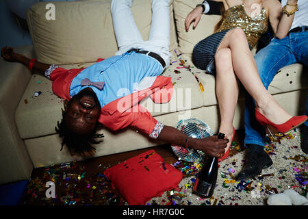 Unkenntlich paar sitzt auf Sofa, während afro-amerikanischer Mann liegend Kopf mit geschlossen Augen und halten Champagner Flasche in der hand Stockfoto