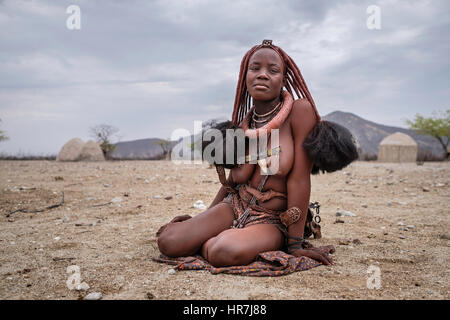 Porträt einer Himba-Frau sitzt auf dem Boden in einem kleinen Dorf. Himbas sind ein Bantu Stamm, wanderten nach heutigen Namibia ein paar Jahrhunderte ist, ein Stockfoto