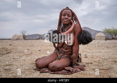 Porträt einer Himba-Frau sitzt auf dem Boden in einem kleinen Dorf. Himbas sind ein Bantu Stamm, wanderten nach heutigen Namibia ein paar Jahrhunderte ist, ein Stockfoto