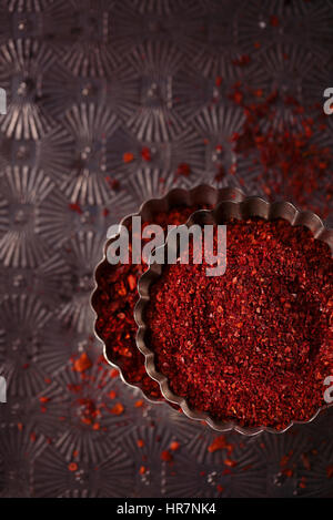 rote heiße Chili Pfeffer Flocken in Vintage Schimmel Zinn auf strukturierten Metall Hintergrund Stockfoto