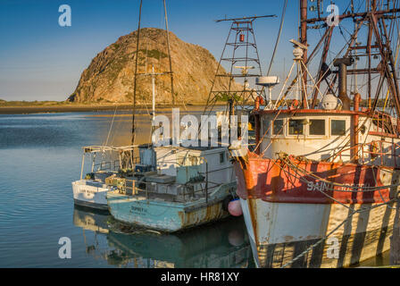 Fischerboote, die bei Sonnenaufgang am Pier in der Nähe des Morro Rock Monoliths festgemacht sind, Blick vom Embarcadero Waterfront Boulevard in Morro Bay, Kalifornien, USA Stockfoto