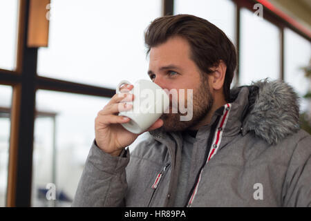 Nachdenklicher Mann tragen warme Winterjacke aus dem Fenster schaute und Kaffee trinken. Stockfoto