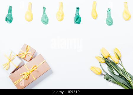 Gelbe Blumen, Geschenk-Boxen mit Bögen und Luftballons auf weißem Hintergrund, Ansicht von oben Stockfoto