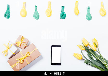 Gelbe Tulpen, Handy, Geschenkboxen mit einer Bändern und Luftballons auf einem weißen Tisch, Ansicht von oben Stockfoto