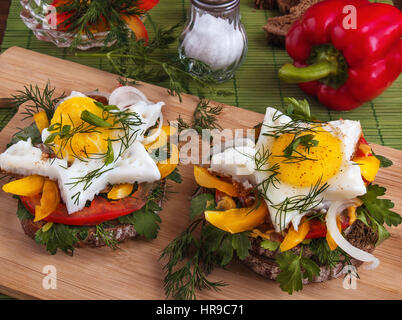 Sandwich mit Spiegeleier auf Brot mit Gemüse, Paprika, Tomaten, Senf, Petersilie, Dill und Zwiebeln auf einem Holzbrett zum Abendessen vorbereitet Stockfoto