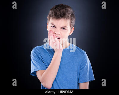 Lässige Kerl haben Zahnschmerzen, auf schwarzem Hintergrund. Emotionales Porträt teenboy - trauriges Kind mit Zahnschmerzen. Zahnprobleme - Teenager leiden unter t Stockfoto
