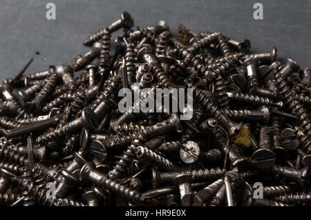 Techno-Hintergründe - schwarz geölt Haufen Schrauben auf einem dunklen grauen Karton Stockfoto