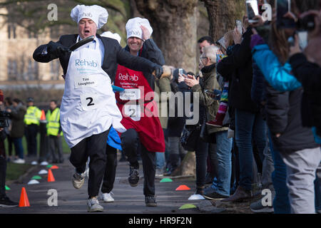 MP für East Worthing und Shoreham Tim Loughton (links) und Journalist George Parker beteiligen sich die jährliche Reha parlamentarischen Pancake Race in der m/s, Lords und Mitglieder der Medien-Rasse, die einander auf Fastnacht um Geld für die Nächstenliebe der Reha, in Victoria Tower Gardens, London. Stockfoto