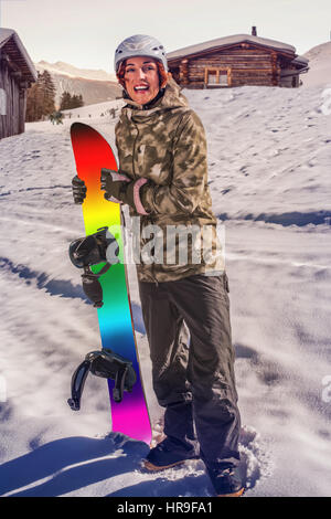 Rothaarige Frau mit Snowboard in der Hand im Schnee vor der Holzhütte Stockfoto