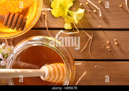 Glas mit Honig und Waben in eine Glasschüssel auf einem braunen Holztisch mit Blumen und Blütenpollen. Ansicht von oben. Horizontale Komposition Stockfoto