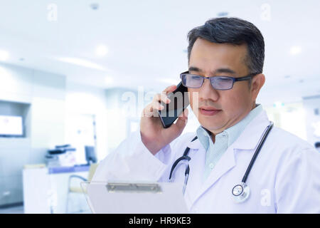 Arzt mit Handy und mit Blick auf Patientenakte in High Key Ton Stockfoto