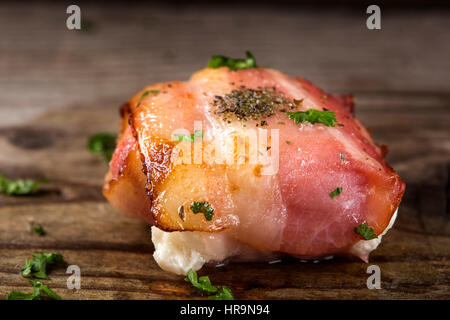 Nahaufnahme von gebratenen Ziegenkäse eingewickelt in Speck auf Holz mit Petersilie Stockfoto