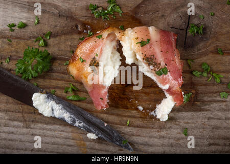 Gebratener Ziegenkäse eingewickelt in Speck auf Holz mit Messer und Petersilie Stockfoto