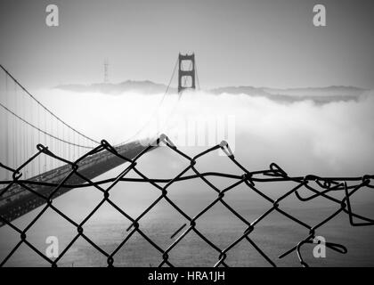 Panoramablick auf die westliche Spanne von der Golden Gate Bridge an einem nebligen Wintermorgen von Batterie Spencer durch einen Zaun, ein Fort Baker Website betrachtet Stockfoto