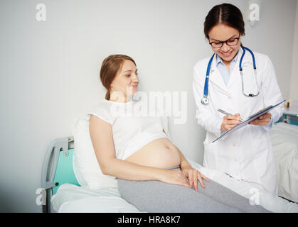 Junge schwangere Frau ruht im Krankenzimmer während ihr Arzt über gute Analysen Ergebnisse sprechen und Lächeln Stockfoto