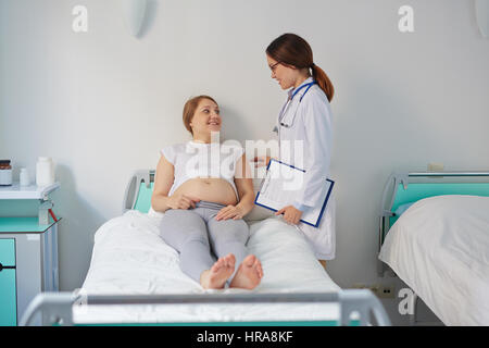 Weiblichen Gynäkologen mit freundlichen Gespräch mit ihrer schwangeren Patientin im Bett liegend und lächelnd Stockfoto