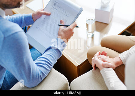 Reife Psychiater sitzt neben seiner Patientin und ihre Fragen notwendig für die Ausfüllung der Gesundheitskarte, close-up erschossen Stockfoto