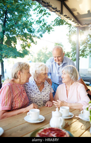 Senioren Freunde Tea-Party im schönen Sommer-Café und teilen Neuigkeiten mit einander, zwei Frauen, die jeweils anderen Schultern Arme aufsetzen Stockfoto