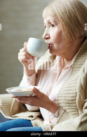 Profil Porträtaufnahme nachdenklich im Ruhestand Frau in Jeans und rosa Hemd Kaffee mit Gebäck im kleinen café Stockfoto