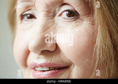 Close-up Portrait faltige senior Frau mit tiefen braunen Augen Blick in die Kamera und lächelnd leicht gedreht Stockfoto