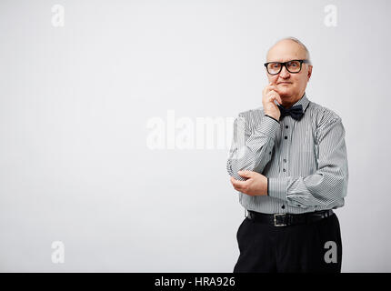 Porträt des eleganten pensionierte Menschen in gestreiften Hemd mit Fliege hält seine Hand am Kinn und Blick in die Kamera sorgfältig Stockfoto