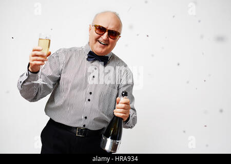 Porträt von stilvollen älterer Mann im gestreiften Hemd mit Fliege hält ein Glas Champagner, einen Toast zu machen und glücklich lächelnd Stockfoto