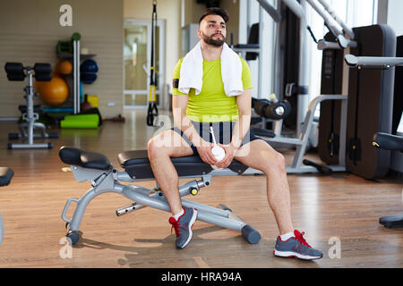 Arbeiten im Fitness-Studio: schöner muskulöser Mann tragen helle grüne Sportsclothes, sitzen auf verstellbare Bank ausruhen nach dem Training mit Maschinen Stockfoto