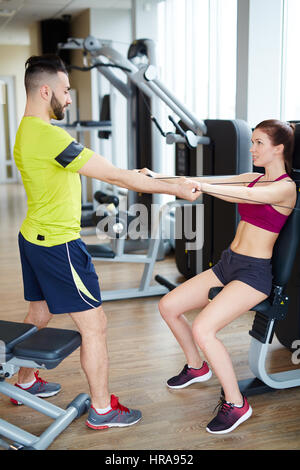 Arbeiten im Fitness-Studio: persönliche Fitness Instruktor Heping junge Frau korrigiere Hebelarm Übung auf Kabel-Rechner Stockfoto