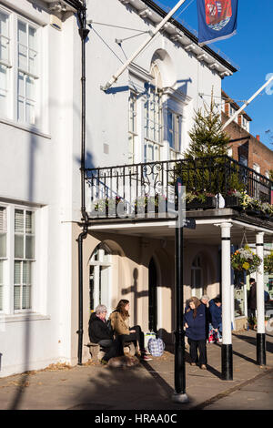 Eine Gruppe von Menschen warten auf einen Bus, unter der Veranda von Tenterden Rathaus in der Wintersonne, Kent, UK Stockfoto