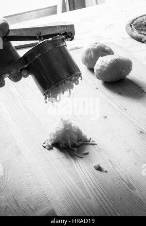 Hände mit einem Kartoffelstampfer, die Zubereitung von Kartoffelgnocchi in einer rustikalen Küche mit natürlichem Sonnenlicht Stockfoto