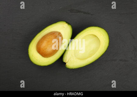 Eine frische reife Avocado Grünschnitt in zwei Hälften mit Grube Stein auf Schiefer Tafel Hintergrund, Detail, Nahaufnahme, erhöht, Ansicht von oben Stockfoto