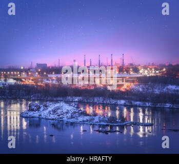 Night cityscape with colorful purple sky with stars, rocks, river, trees, buildings, city illumination and steel factory with smokestack in winter Stockfoto