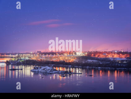 Night cityscape with colorful purple sky with stars, rocks, river, trees, buildings, city illumination and steel factory with smokestack in winter Stockfoto