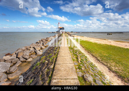 Pflasterweg führt zum Leuchtturm an der Küste auf dem Hintergrund der blaue Himmel mit Wolken bei Sonnenuntergang im Frühling in Niederlande. Landschaft Stockfoto