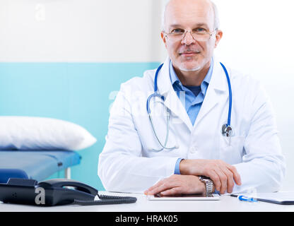 Leitender Arzt an seinem Schreibtisch arbeiten mit medizinischen Geräten in den Hintergrund. Stockfoto