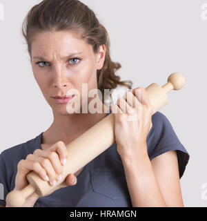 Aggressive Frau hält einen hölzernen Nudelholz und Blick in die Kamera. Stockfoto