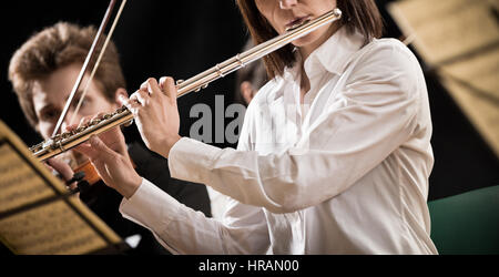 Elegante weibliche Flötist auf der Bühne mit Orchester. Stockfoto