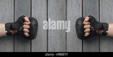 Zwei Männer Hände in schwarze Lederhandschuhe für Thai-Boxen auf grauen getragen hölzernen Hintergrund, ballte die Hände einander gegenüber Stockfoto