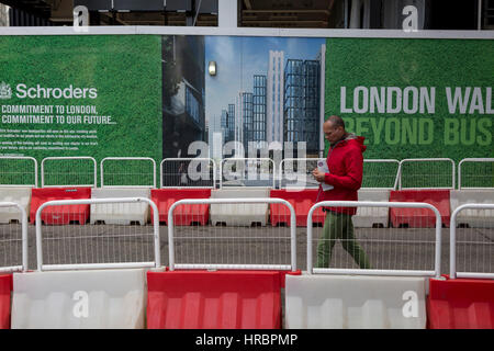 Eine rote und grüne Bau Horten mit einem Fußgänger vorbeigehen tragen identische Farben am 16. Februar 2017, in der City of London, England. Stockfoto