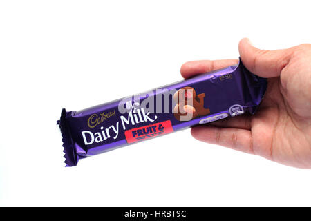 Hand hält Australien Cadbury Frucht und Nuss und Caramello-Schoko-Riegel gegen Kuhmilch Hintergrund isoliert Stockfoto