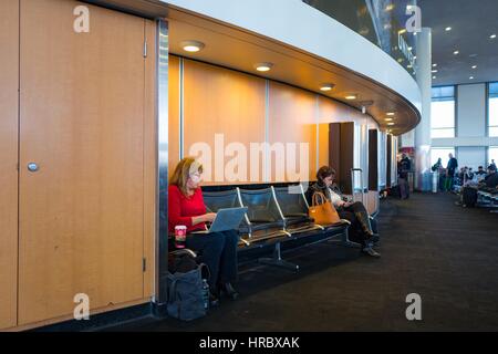 Zwei weibliche Reisende sitzen auf Bänken und arbeiten auf ihren Laptops und Smartphones während des Wartens auf ihre Flüge im Terminal 2 am Los Angeles International Airport (LAX), Los Angeles, Kalifornien, 22. November 2016. Stockfoto