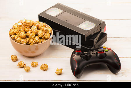 Karamell Popcorn in der Nähe von einem Videoband und Gamepad auf hölzernen Hintergrund Stockfoto