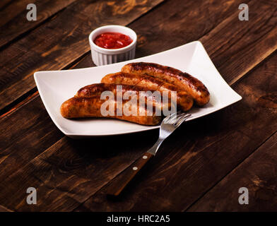 Gegrillte Würstchen mit Sauce Ketchup in einem weißen Teller auf einem Holztisch Stockfoto