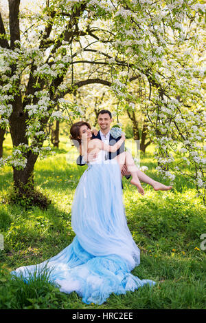 Braut und Bräutigam Mann zusammen halten und heben Sie seine Freundin. Junge Hochzeitspaar umfassend in blühenden Frühling Garten. Liebe und romantische Thema Stockfoto